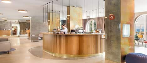 A reception area with a wooden counter, a barista preparing a drink, and a view of the sea through a large window.