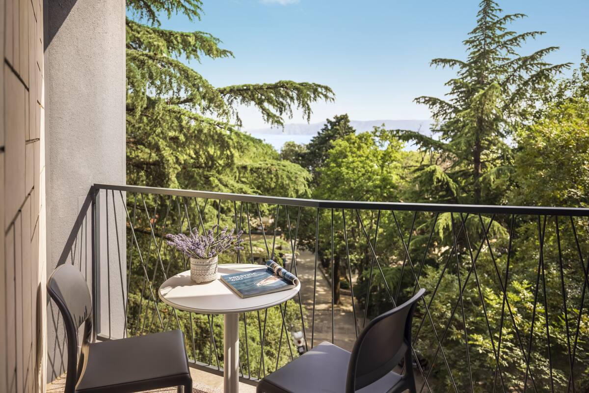 A balcony with a table, chairs, and a view of a forested area.