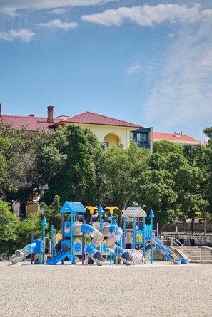 A playground with slides and climbing structures, surrounded by trees and a building with a red roof. - Aminess Vival Casa Lisanj (Delnice)