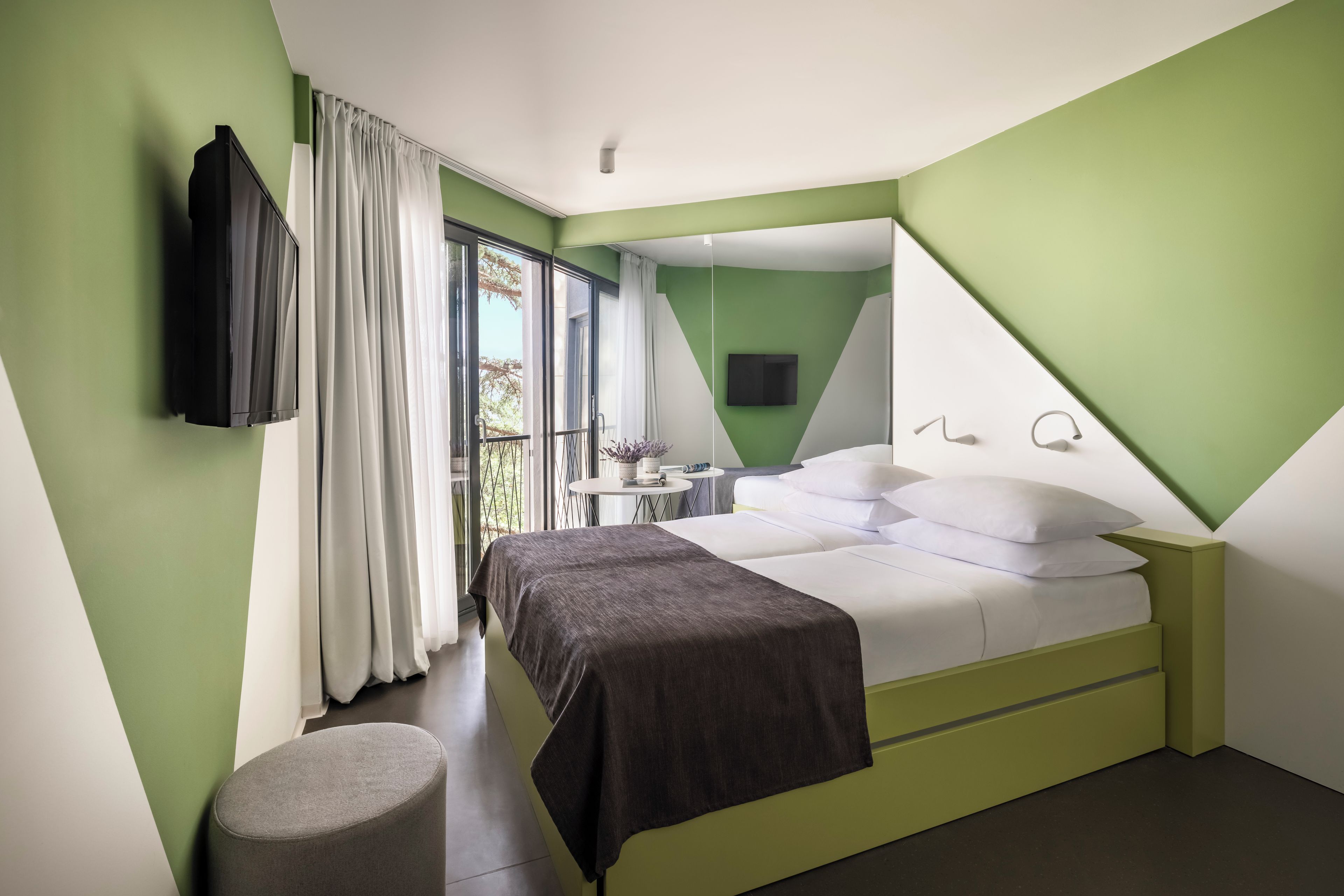Una habitación de hotel moderna con una cama, televisión, una mesita y una ventana con cortinas.