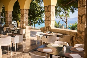 Un espace extérieur aménagé pour les repas, avec des colonnes en pierre, des chaises et des tables en osier, le tout préparé pour accueillir les convives.