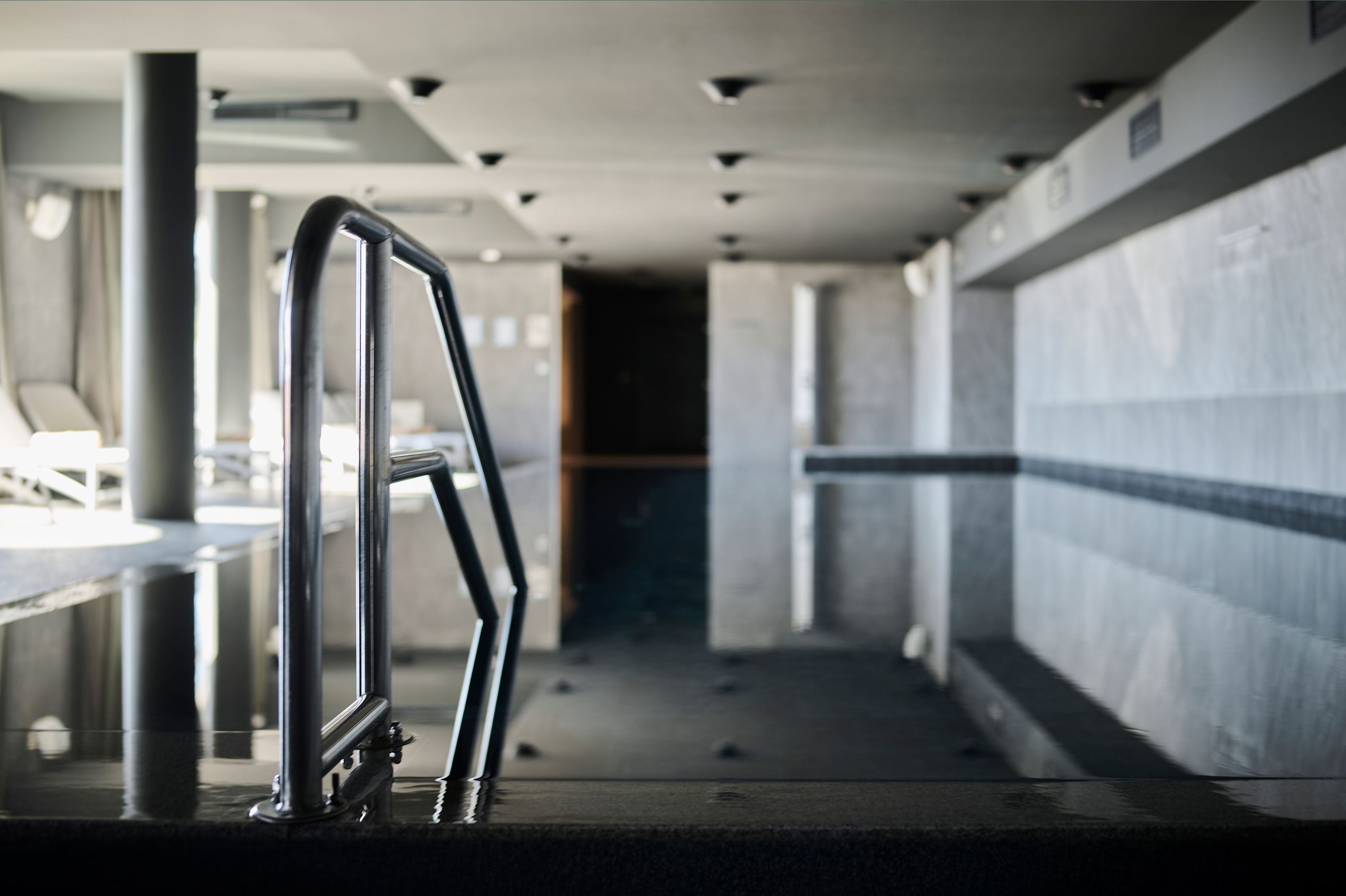 A clean, modern indoor space with a metal handrail, a bench, and a tiled wall.
