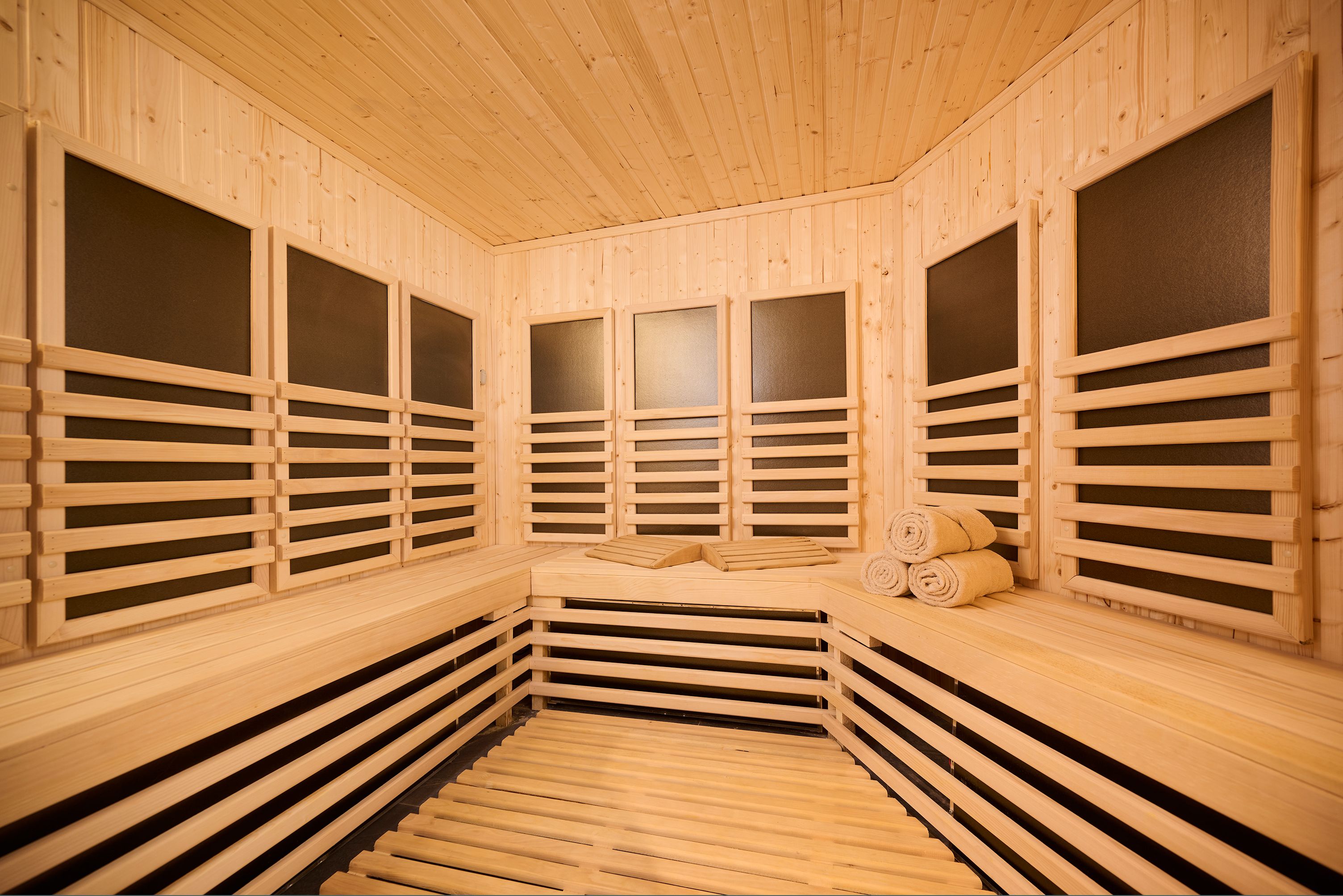Un sauna avec des murs et des bancs en bois, un banc avec des serviettes et un autre banc avec une serviette.