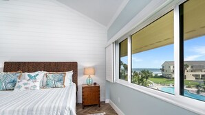 Ein Schlafzimmer mit Bett, Nachttisch, Lampe und Blick auf Pool und Gebäude.