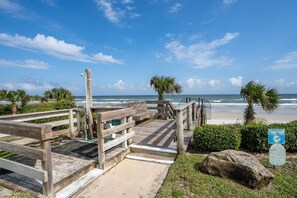 A wooden boardwalk leading to a beach with palm trees and a sign indicating lights out for sea turtles.