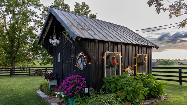 A rustic wooden cabin with a sloped roof, surrounded by a stone border and lush greenery. -  Farmhouse in the Country-Perfect Place to Relax and Enjoy Family and Friends! (Lebanon)