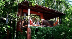 Una pequeña estructura de madera, elevada y con balcón, rodeada de frondosa vegetación tropical.