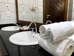 A bathroom with two sinks, a mirror, and a towel rack with folded towels. - Hotel Portaló (Cairu)