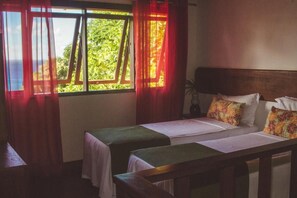 Une chambre avec deux lits, une fenêtre avec des rideaux et une tête de lit en bois.
