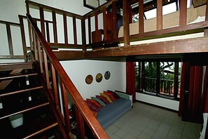 Un intérieur à plusieurs niveaux avec un escalier en bois, un canapé agrémenté de coussins colorés et un balcon offrant une vue panoramique.