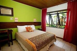 A room with a bed, a desk, a window with red curtains, and a green wall. - Hotel Portaló (Cairu)