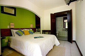 Un dormitorio con una cama, una mesita de noche, una ventana y un baño visible a través de una puerta abierta.