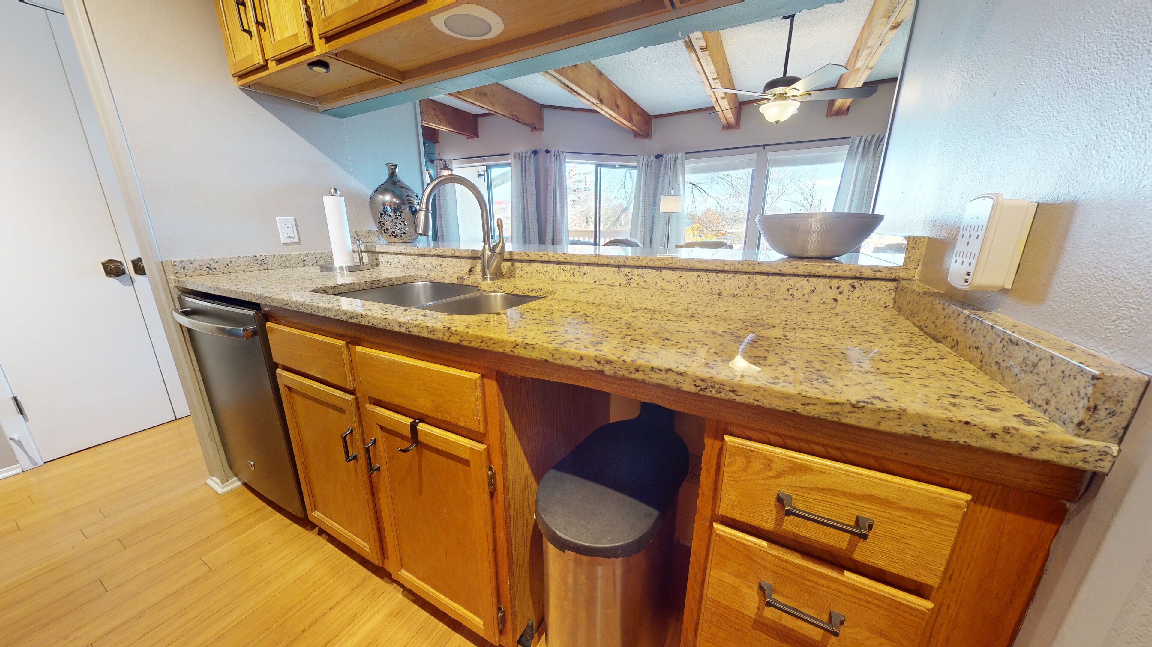 A kitchen with wooden cabinets, a granite countertop, a stainless steel sink, and a ceiling fan.