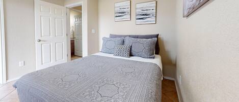 Un dormitorio con una cama grande, dos cuadros colgados en la pared y una puerta que da a otra habitación.