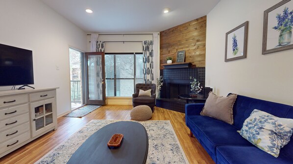 A living room with a TV, a blue sofa, a fireplace, and a wooden wall.