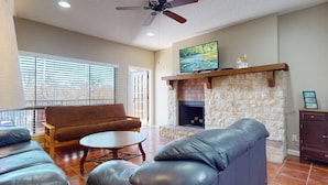 A living room with a stone fireplace, a sofa, a leather chair, and a television mounted above the fireplace. - River City Resorts: C202 along the Comal River (New Braunfels)