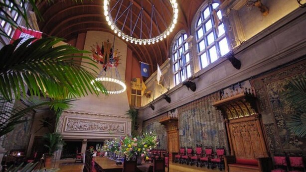 Un salón imponente con techos altos, candelabros ornamentales y un gran arreglo floral en el centro.