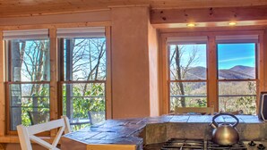 Cocina rústica de cabaña con encimera de piedra, estufa a gas y ventanas amplias con vistas a las montañas.