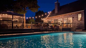 Ein Schwimmbad mit Lichterketten, Sitzgelegenheiten im Freien und einer überdachten Terrasse.