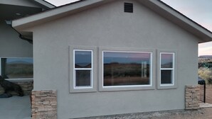 Een modern huis met een stenen gevel, drie ramen en uitzicht op het woestijnlandschap.