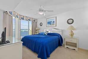 Quarto de hotel com uma cama grande, um ventilador de teto, vista para o oceano, uma escrivaninha com telefone e uma mesa de cabeceira com abajur.