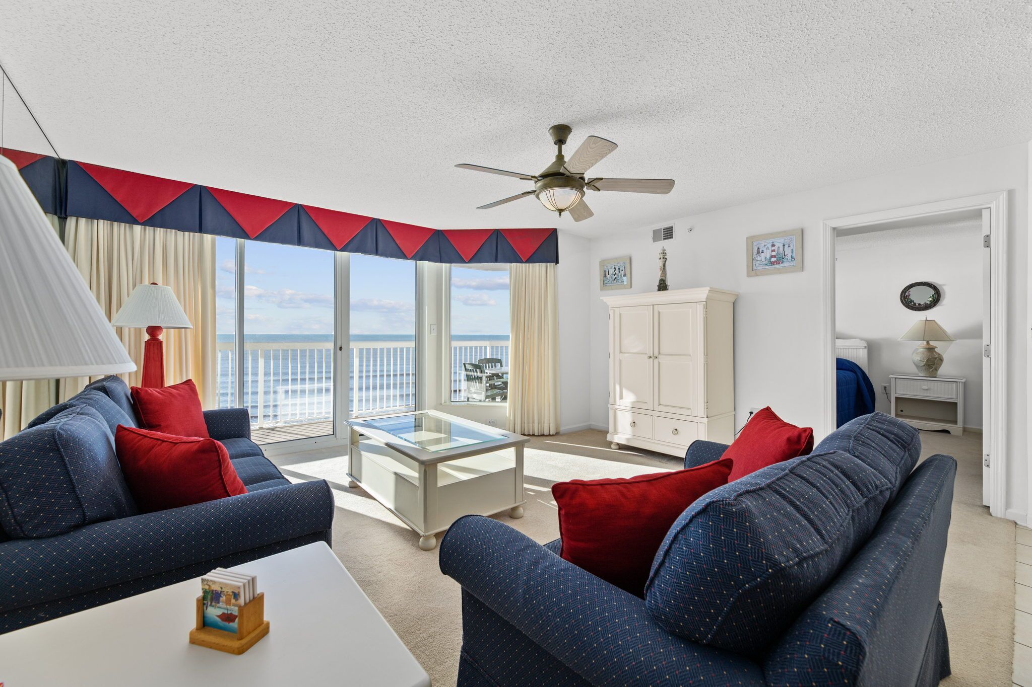 A living room with a sofa set, a glass coffee table, and a view of the sea through large windows.