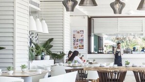 Un restaurante moderno con paredes blancas, mesas de madera y lámparas colgantes.