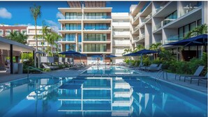 Un hotel moderno con zona de piscina, varios balcones y tumbonas.