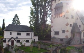 Un bâtiment blanc avec un toit noir, entouré de verdure et d’un petit étang.