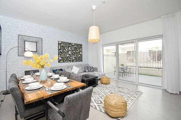 A modern living room with a dining area, a sofa set, a large window, and a balcony.