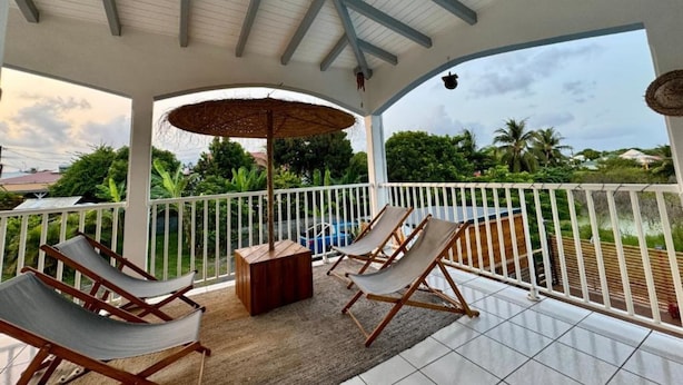 A covered outdoor area with two lounge chairs, a wooden table, and a thatched umbrella.