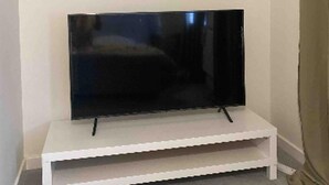 A flat-screen TV on a white stand in a room with plain walls and a carpeted floor.