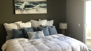A bedroom with a large bed, a ceiling fan, a painting of waves, and a window. - Beachee Townhouse  (San Diego)