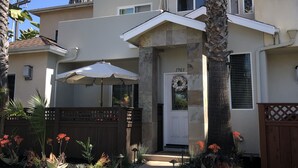 A two-story house with a stone facade, a white door with the number 1903, and a covered patio area. - Beachee Townhouse  (San Diego)
