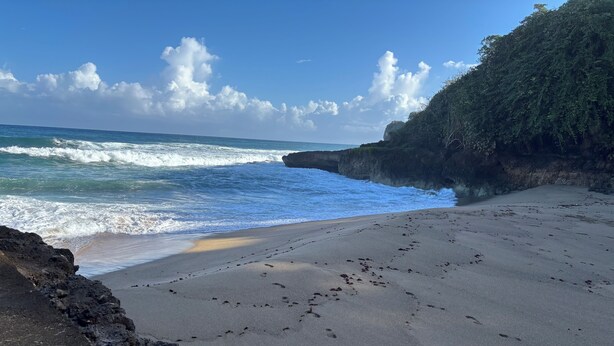 A beach with footprints leading to the water, a rocky cliff, and a clear sky. - Private Villa, Ocean & Mountain view with Solar Heated Pool. (Quebradillas)