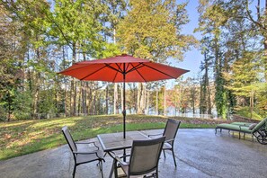 Une terrasse extérieure avec une table et des chaises, un parasol rouge et une vue sur une forêt et un lac.