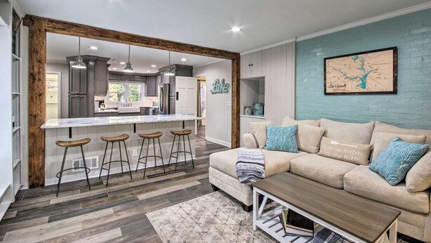 Una cocina moderna con taburetes de bar, un comedor con sofá y mesa de centro, y un mapa colgado en la pared.