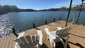 Una terraza de madera con dos sillones Adirondack blancos que dan a un lago tranquilo.
