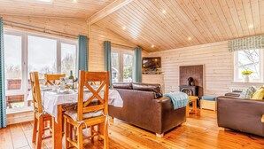 Un acogedor interior de cabaña con pisos de madera, una zona de comedor con mesa y sillas, un sofá y una chimenea.
