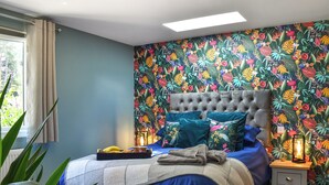 Quarto com cabeceira estofada, cama com roupa de cama azul, bandeja com frutas e mesa de cabeceira com abajur.