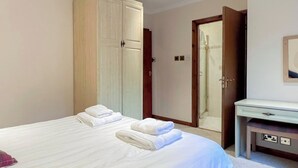 A hotel room with a large bed, a wardrobe, a bathroom with a shower, and a small vanity table.