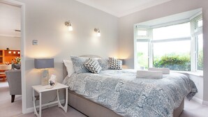 A bedroom with a large bed, bedside tables, a nightstand, and a window with a view of greenery. - Leighwood Cottage is perfect for a romantic getaway. (Paignton)