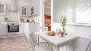 A modern kitchen with white cabinetry, a built-in oven, and a dining area with a white table and chairs. - Leighwood Cottage is perfect for a romantic getaway. (Paignton)