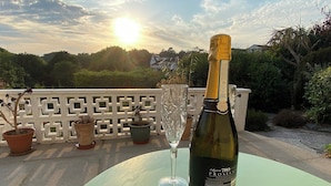 A bottle of wine on a table with a glass, surrounded by potted plants and a white fence. - Leighwood Cottage is perfect for a romantic getaway. (Paignton)
