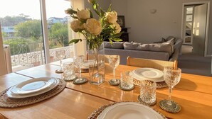 A dining table set with plates, glasses, and a vase of flowers, with a view of the outdoors through large windows. - Leighwood Cottage is perfect for a romantic getaway. (Paignton)