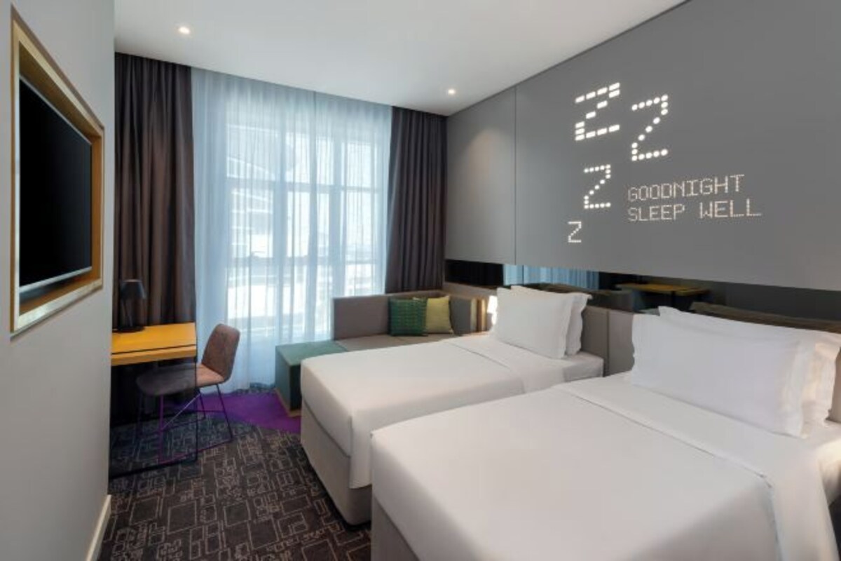 A hotel room with two beds, a desk, a chair, and a large window with curtains.