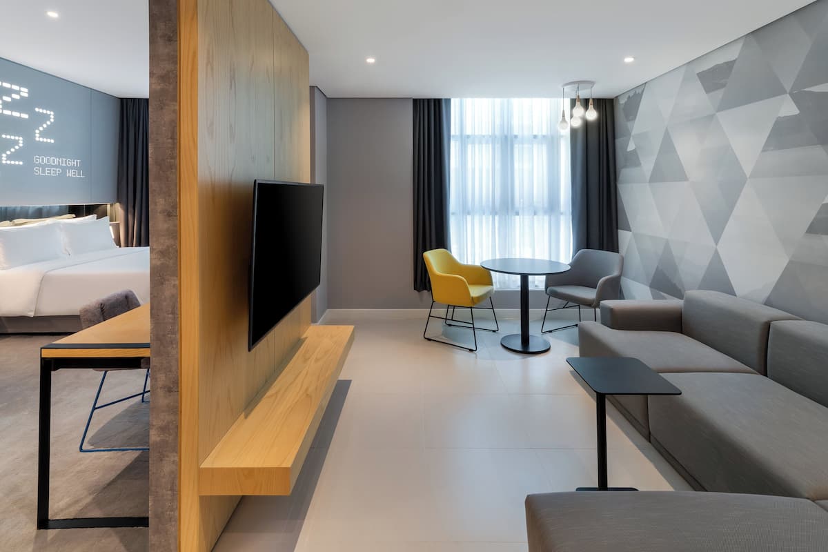 Una habitación de hotel moderna con cama, televisión, sofá, una mesita y dos sillas.