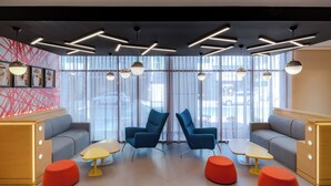 A modern lounge area with sofas, chairs, and ottomans, featuring geometric ceiling lighting and large windows.