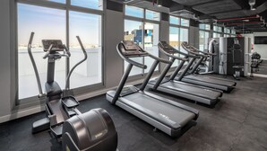 A gym with treadmills, ellipticals, and weight machines, large windows with a city view, and a modern industrial design.