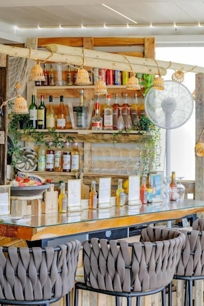 A bar area with wooden shelves stocked with bottles, a glass bar counter, and woven chairs. - Victoria Boutique Hotel (Arcachon)